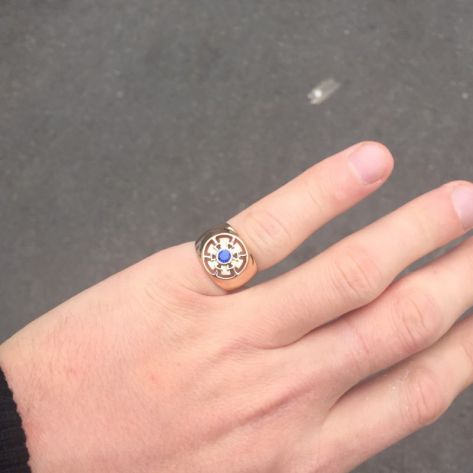 мужская печатка с одним камнем в красном золоте и синим камнем на пальце вдалеке